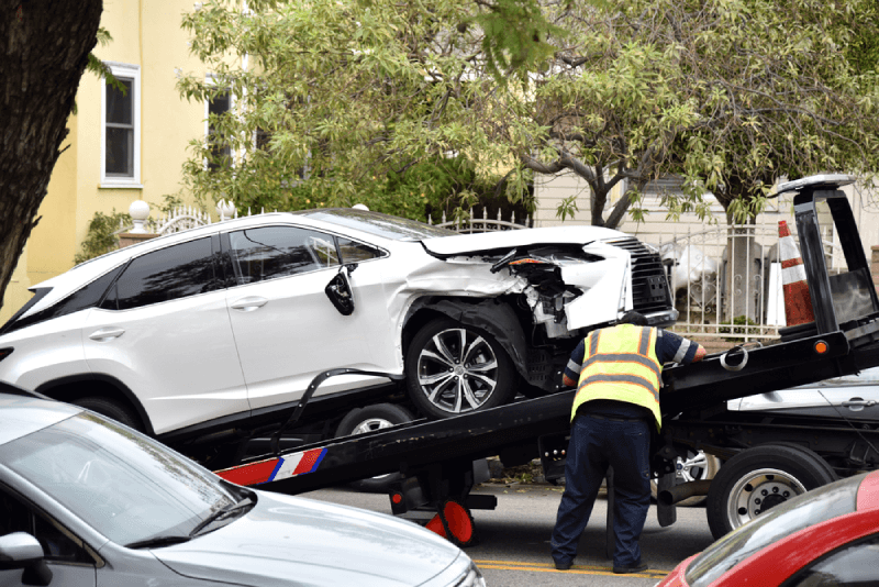 damage white car with towing personnel on the road