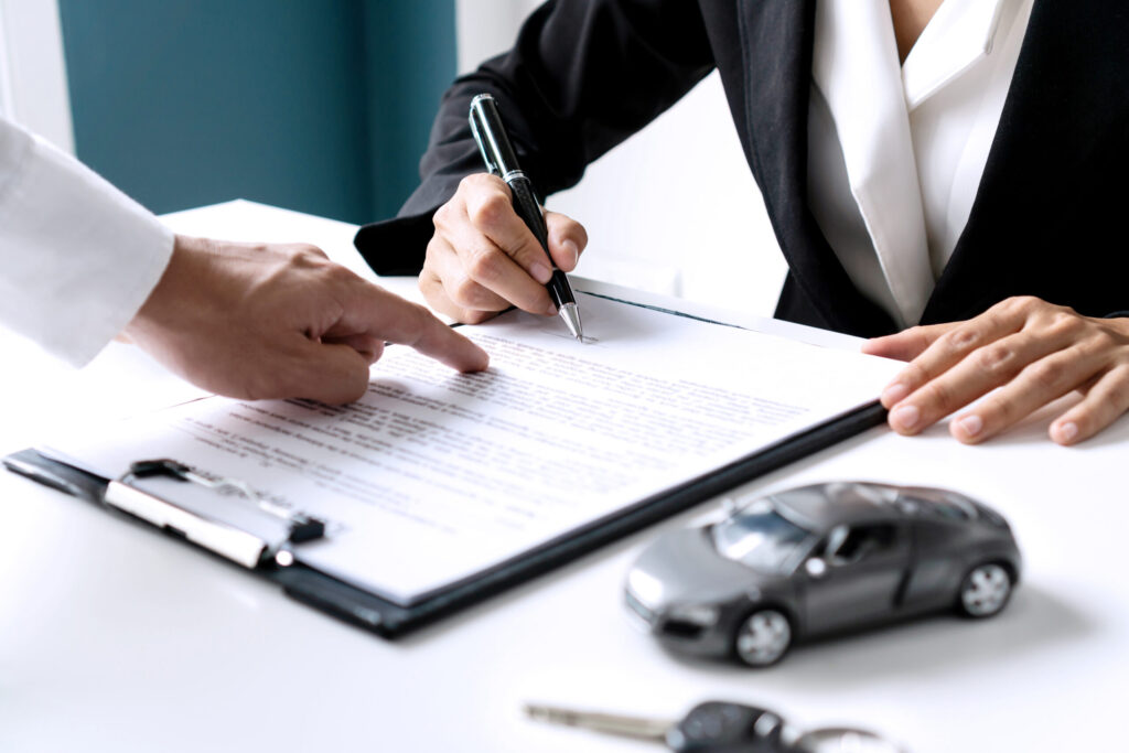 Closeup of Asian female signing car insurance document or lease paper contract or agreement. Buying or selling new or used vehicle with car keys on table.
